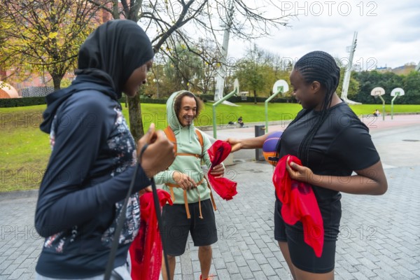 Diverse friends on an urban basketball court smiling and holding red pennants, preparing to play outdoors casual, multicultural young adults enjoying teamwork and fun together