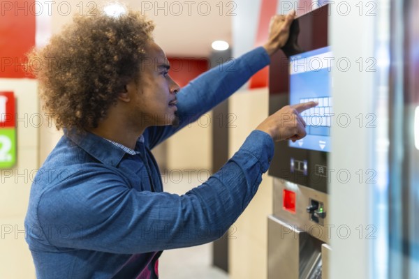 Young man standing, pointing finger at a digital touchscreen on an automated vending machine, making a selection for a drink or snack, representing modern self service convenience and technology