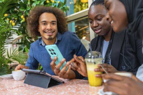 Young diverse friends in a cozy cafe sharing smartphone content, chatting and laughing over coffee and juice, relaxed together with a tablet and casual city vibe energy