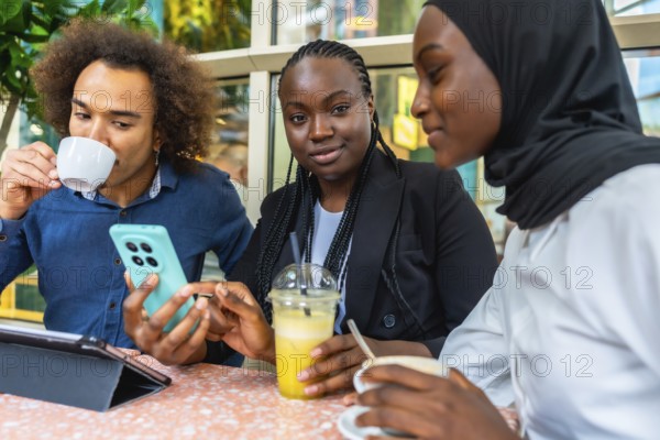 Group of multiethnic young adults relaxing together at a cafe, using a smartphone, discussing content and sharing social connection over beverages and a tablet on the table