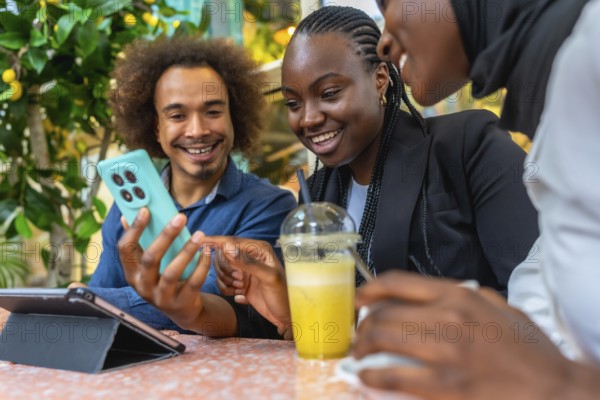 Diverse friends are happily socializing at a cafe, using a smartphone to view and share content, with one person holding a refreshing drink while enjoying technology and connection