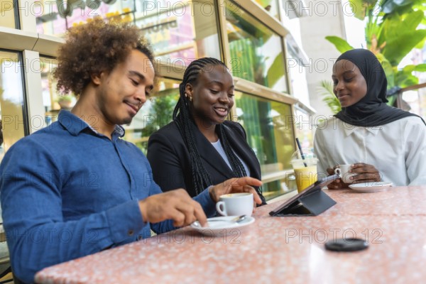 Diverse group of young adult friends enjoying a casual meeting in a modern cafe, sharing information and ideas while looking at a tablet and drinking coffee