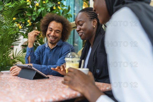 Cheerful diverse friends sitting at a cafe table, laughing and discussing content on a digital tablet while enjoying beverages, representing connection, leisure, and modern social interaction