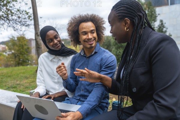 Diverse colleagues discussing and brainstorming ideas while working on a laptop together, highlighting teamwork, education, and modern business collaboration in an outdoor park setting