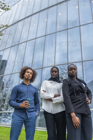 Group of young diverse business professionals standing with confident serious expressions in front of a contemporary glass office building, representing corporate success and global teamwork
