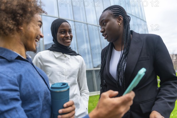 Group of multi ethnic colleagues engaging in a friendly conversation outside a modern office building, sharing ideas and using a mobile device for collaboration