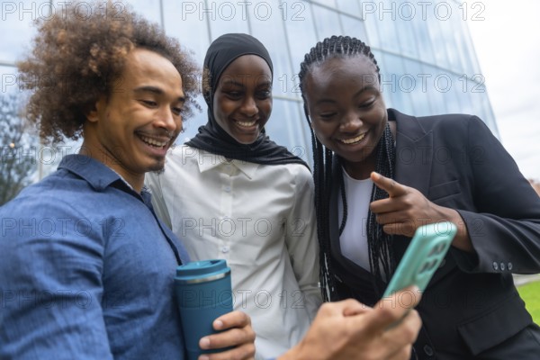 Group of diverse friends standing close together, smiling and laughing while looking at a smartphone screen, sharing a moment of connection outdoors near a contemporary building