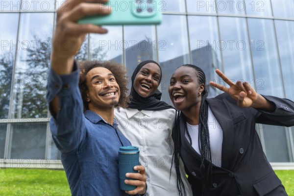 Three diverse friends smiling and laughing while taking a group selfie with a smartphone, celebrating friendship and connection outdoors with modern office buildings in the background