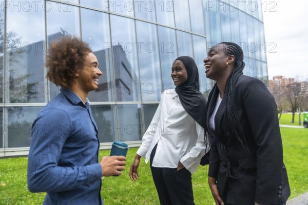 Diverse group of business colleagues, including a man holding a reusable cup and two women, laughing and smiling while standing outdoors in front of a modern glass building