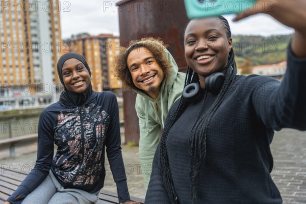 Three smiling diverse young adults enjoying friendship and making a selfie outdoors in an urban setting, wearing activewear and showing cheerful expressions