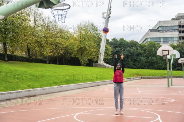 Muslim woman wearing a hijab and sportswear on an urban basketball court shooting a colorful ball, actively engaged in sport, demonstrating inclusivity and athleticism