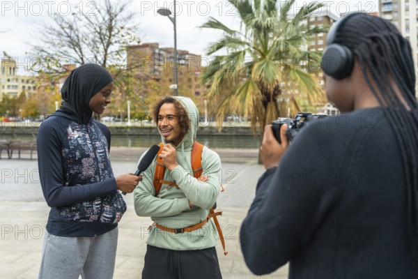 Content creators filming an outdoor interview with a smiling man, capturing diverse perspectives and reporting news for a modern street media production