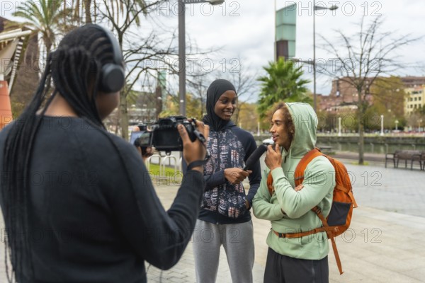 Journalist filming and interviewing a diverse group of young adults in an urban park, capturing candid, authentic news and social media content with camera and microphone