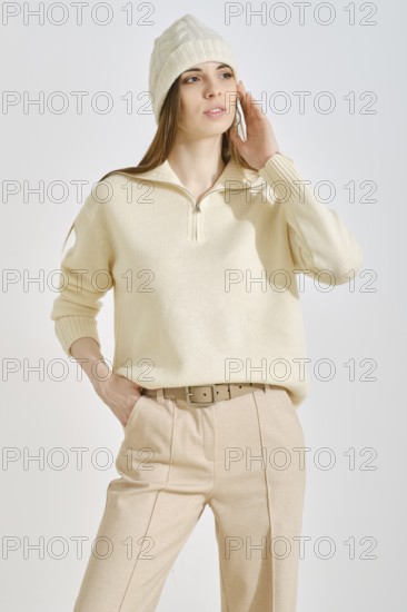 A woman wearing a light cream sweater and beige trousers, perfect for a casual outing. She accessorizes with a matching beanie while posing thoughtfully against a simple backdrop