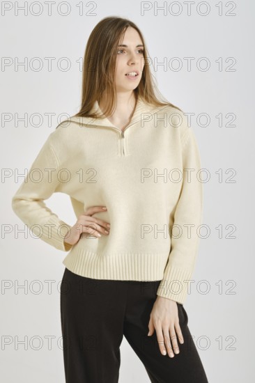 A woman showcases a stylish, cream-colored sweater paired with black trousers in a minimalist setting. This outfit is perfect for spring, blending comfort with contemporary fashion for everyday wear