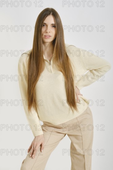 A young woman poses confidently, showcasing a trendy outfit that emphasizes both style and comfort. She stands against a simple backdrop, radiating an effortless charm