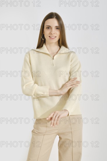 Cheerful woman in a light cream sweater and beige pants posing over white background. The outfit highlights a blend of comfort and fashion, ideal for various activities and settings