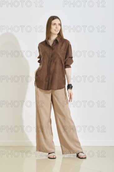 A woman in a trendy brown shirt and beige wide-leg pants posing over white background. Perfect for a casual outing, ideal for warm weather and relaxed activities