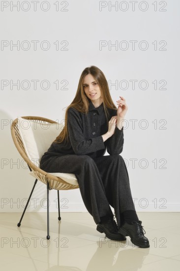 A young woman sits stylishly in a cozy chair, dressed in a trendy, practical outfit that highlights comfort