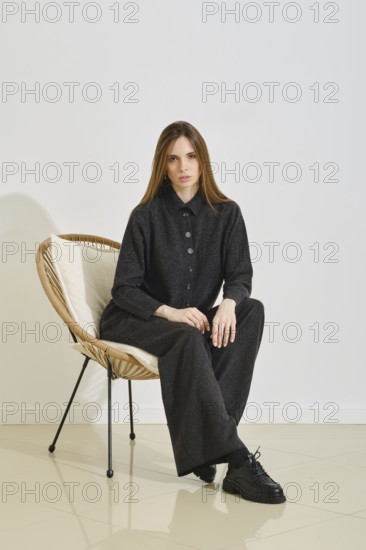 A model sits in a stylish chair, wearing a trendy black shirt and loose pants. Her outfit emphasizes both practicality and comfort