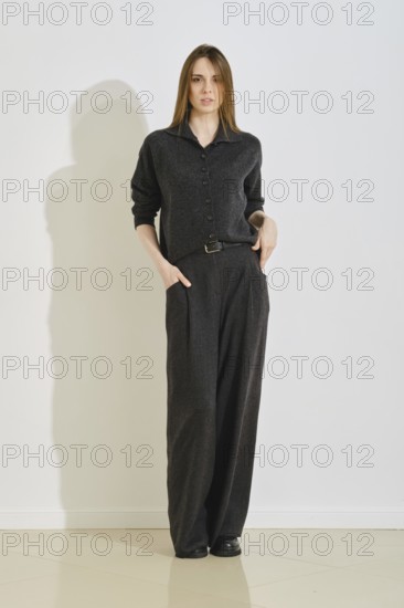 A woman stands in a trendy dark outfit, featuring a button-up top and loose pants. She showcases convenience and style, perfect for a day in the city or casual gatherings