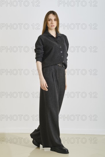 A woman showcases a stylish black ensemble featuring a button-up top and wide-legged pants. Designed for comfort, she stands confidently in a minimalistic indoor space, highlighting modern fashion