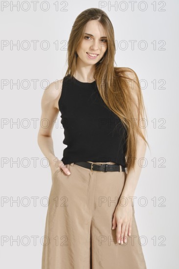 A woman stands confidently in a trendy female outfit, featuring a black tank top and beige wide-leg pants. The look combines convenience and practicality, perfect for casual outings