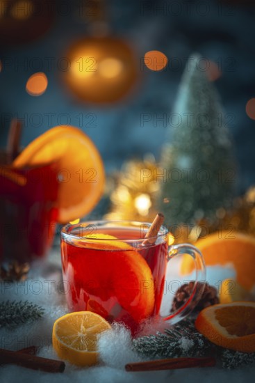 A glass of mulled wine with oranges and cinnamon, golden lights and Christmas decorations in the background