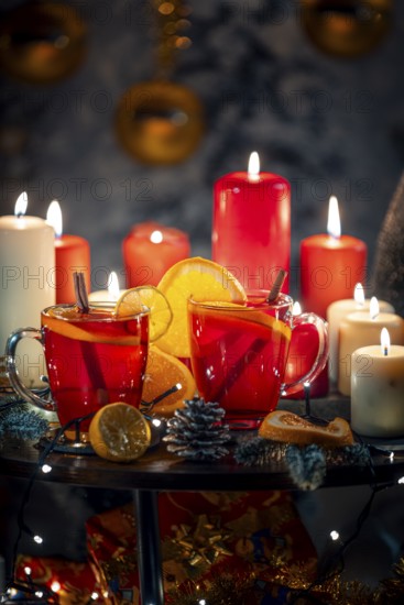 Two glasses of mulled wine with cinnamon and oranges in front of red and white candles, Christmas atmosphere