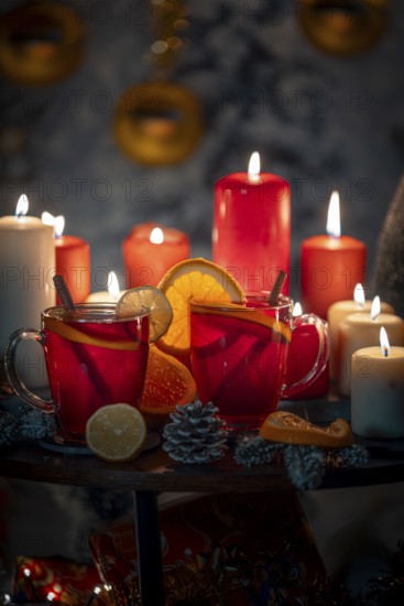 Hot mulled wine with cinnamon sticks and oranges on a Christmassy background with candles