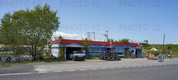 Auto repair shop next to the road with stacked tires and vehicles surrounded by quiet countryside, Lake Sevan car repair shop, Gegharkunik province, Armenia