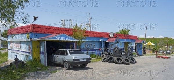 Auto repair shop with stacked tires and vehicles surrounded by rural surroundings under blue skies, Lake Sevan car repair shop, Gegharkunik province, Armenia