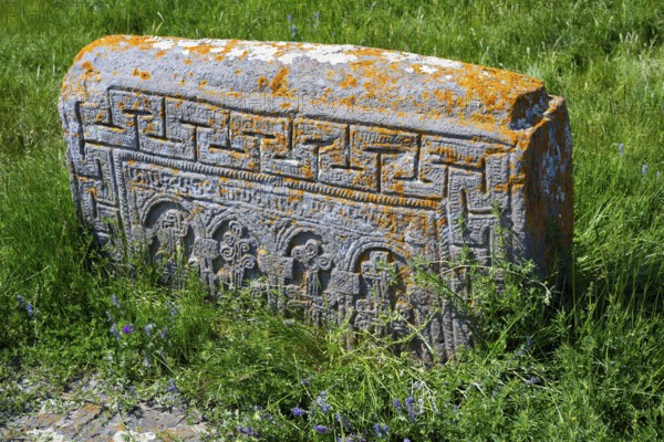 Ancient tombstone set in grass with complex carvings and orange patina, Noratus cemetery, Noradus, Gegharkunik province, Armenia