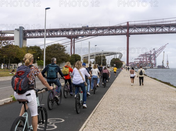 Cyclists on Ponte 25 de Abril, 3.2 km long bridge in Portugal with a 2278 meter long suspension bridge across the Tagus, cloudy and rainy weather, third-longest suspension bridge with combined road and rail traffic, Lisbon, Portugal