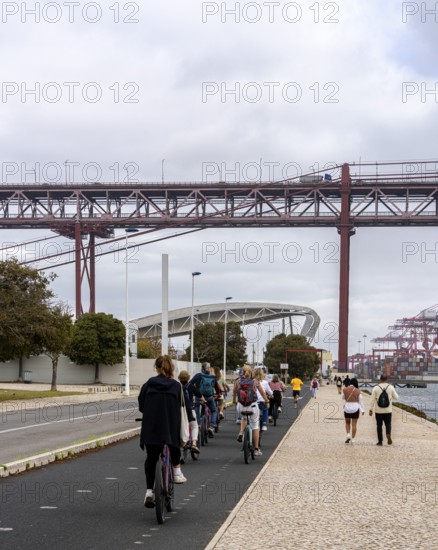 Cyclists on Ponte 25 de Abril, 3.2 km long bridge in Portugal with a 2278 meter long suspension bridge across the Tagus, cloudy and rainy weather, third-longest suspension bridge with combined road and rail traffic, Lisbon, Portugal