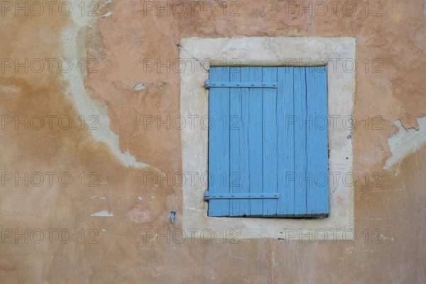 A dilapidated, blue-painted shutter on a faded wall, village of Menerbes, Luberon, Vaucluse, Provence, France