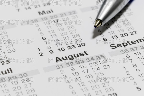 Close-up of a calendar with ballpoint pen pointing to the month of August