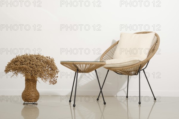 A cozy chair with soft cushioning sits next to a small, stylish table in a contemporary living area. A decorative vase filled with dried flowers adds a touch of nature to the warm design