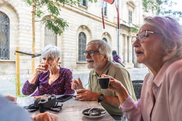Group of diverse senior friends smiling and interacting socially while drinking coffee at an outdoor cafe table in a city, living an active lifestyle and celebrating aging gracefully
