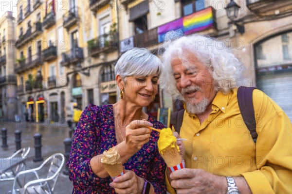 Happy senior couple sharing ice cream while sightseeing in a european city, smiling together with a rainbow pride flag in the background celebrating love and travel