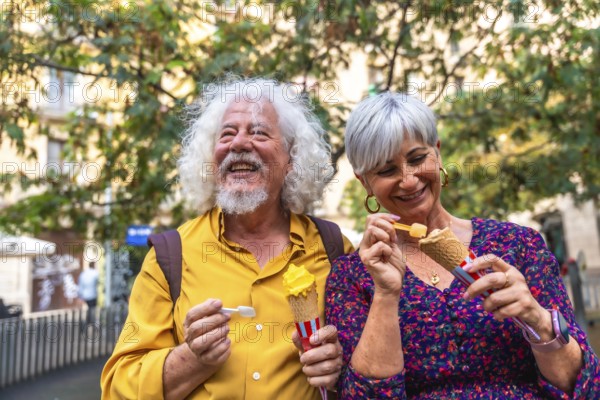 Smiling senior couple sharing an outdoor date, happily eating ice cream cones, representing active lifestyle, love, and joy in their golden years during a summer urban outing