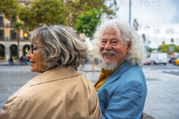 Senior couple walking in an urban environment, the man happily turning and smiling at the camera while his wife looks forward, portraying joy and companionship in their active lifestyle