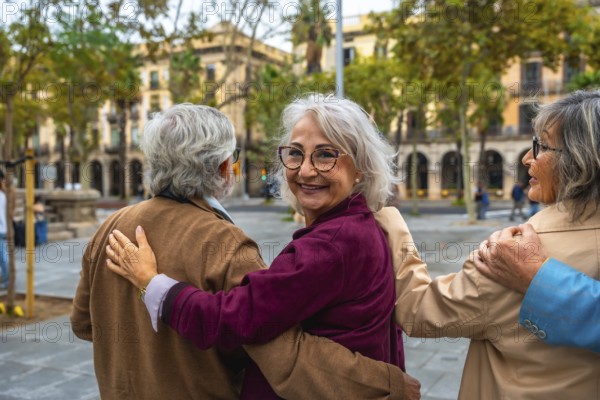 Group of three joyful senior friends walking together, hugging, and smiling at the camera in an urban public square, enjoying their shared bond and companionship
