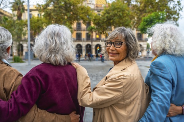 Senior friends walking together in an urban setting, the woman with glasses turning back, smiling at the camera, symbolizing togetherness, vitality, and active aging