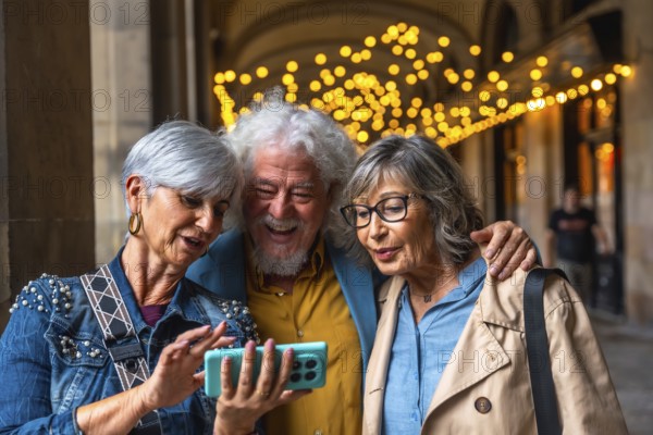 Three happy senior friends standing outdoors, looking at a smartphone screen, interacting with technology while sharing genuine laughter and enjoying time together in a city environment