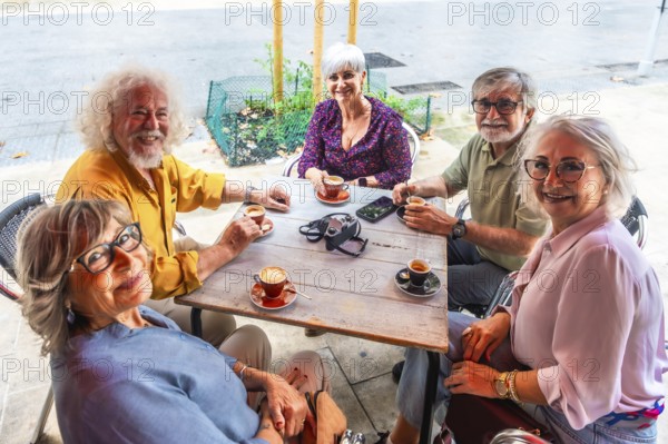 Smiling group of senior friends gathered around an outdoor cafe table, enjoying coffee, conversation and relaxed togetherness on a sunny city day, diverse and joyful