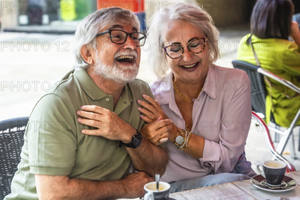 Mature couple laughing and chatting over coffee on a sunny outdoor cafe patio, enjoying relaxed conversation, companionship and carefree retirement moments together