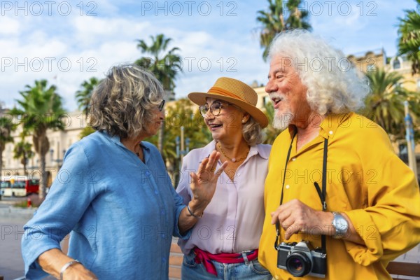 Three cheerful senior friends enjoying a lively discussion outdoors during their city vacation, sharing laughter and good times under palm trees and a bright sky