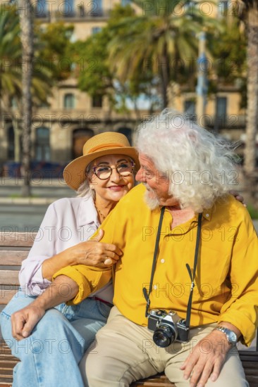 Smiling senior woman embracing her husband on a bench, having a happy moment during their exciting travel adventure in a vibrant european city with palm trees and historic architecture