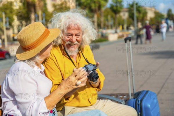 Happy senior couple sitting on a bench in a sunny european city, smiling as they examine a vintage film camera during retirement travel and leisurely sightseeing together